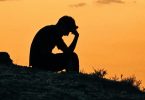 A person sitting alone in silhouette against a sunset sky