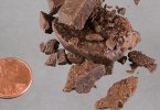 Chunks and crumbs of pressed brown hashish beside a US penny for scale