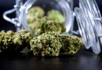 Cannabis flower beside a tipped glass storage jar